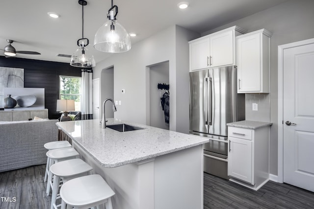 kitchen featuring sink, light stone counters, a center island with sink, stainless steel fridge, and white cabinets