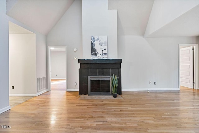 unfurnished living room featuring wood finished floors, visible vents, baseboards, high vaulted ceiling, and a fireplace