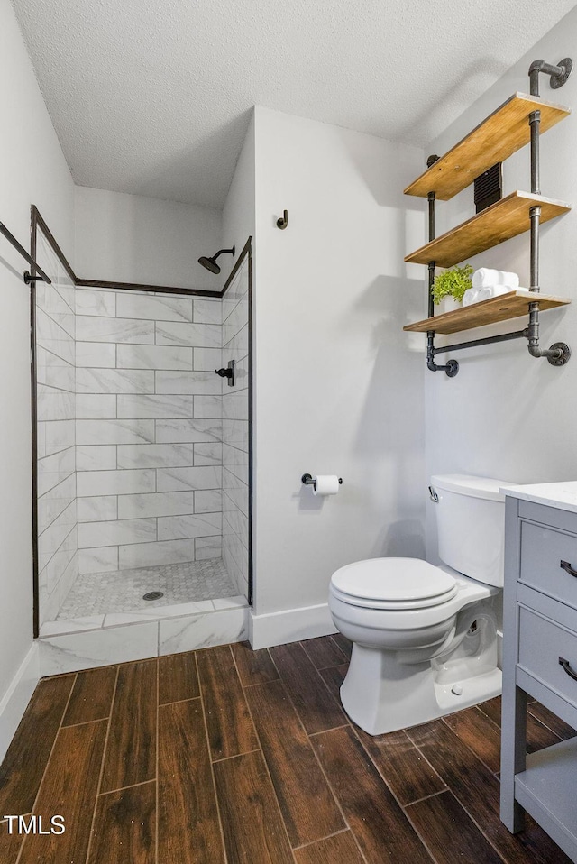 bathroom with wood finish floors, toilet, a textured ceiling, a tile shower, and baseboards