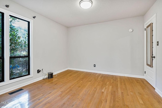 empty room with light wood-type flooring, visible vents, baseboards, and a textured ceiling