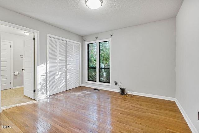 unfurnished bedroom with baseboards, visible vents, a closet, wood-type flooring, and a textured ceiling