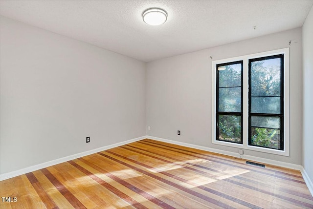 empty room featuring visible vents, light wood-style flooring, a textured ceiling, and baseboards