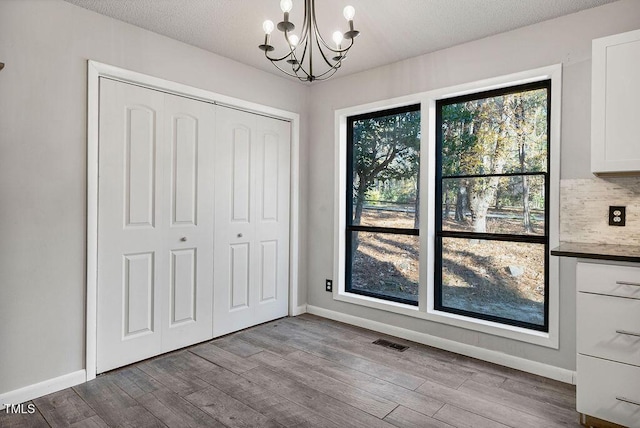 unfurnished dining area featuring a textured ceiling, a notable chandelier, and light wood-type flooring