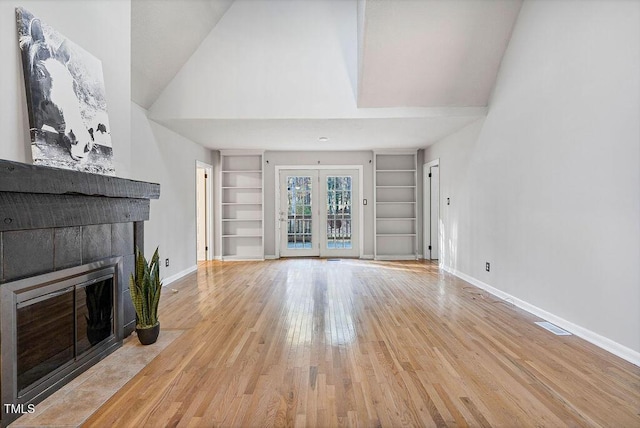 unfurnished living room featuring built in shelves, french doors, wood-type flooring, baseboards, and a tile fireplace