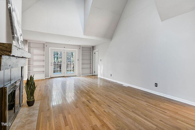 unfurnished living room with a tile fireplace, high vaulted ceiling, light hardwood / wood-style floors, and built in shelves