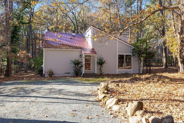 mid-century home with metal roof, gravel driveway, and entry steps