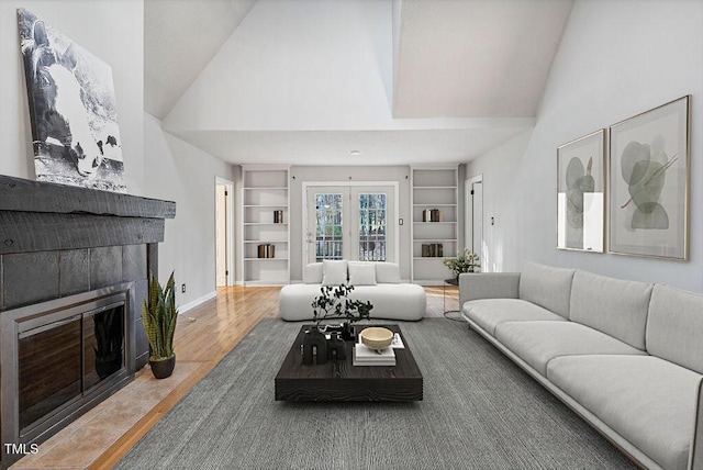 living room featuring built in shelves, baseboards, a tile fireplace, wood finished floors, and high vaulted ceiling