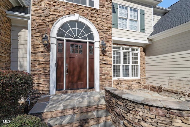 entrance to property featuring stone siding and a shingled roof