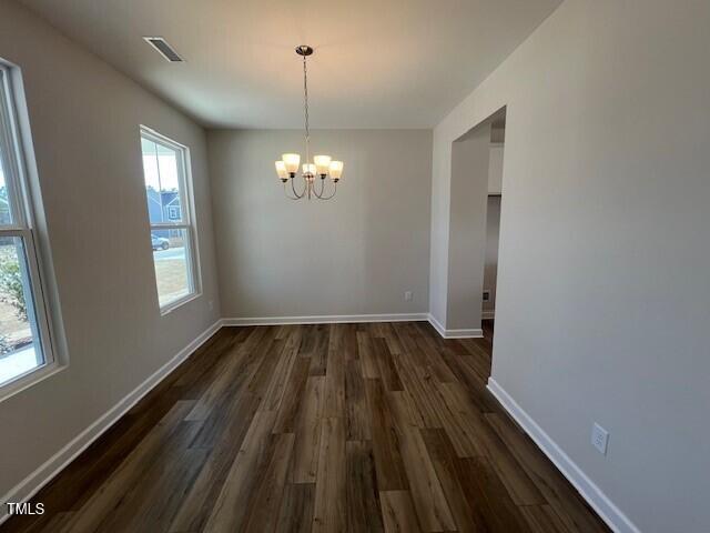 unfurnished dining area featuring baseboards, dark wood-type flooring, visible vents, and an inviting chandelier