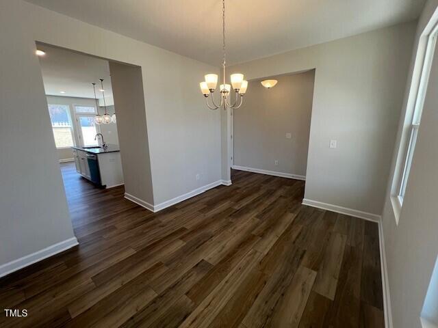 unfurnished dining area with an inviting chandelier, baseboards, dark wood-type flooring, and a sink