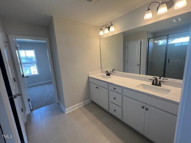 bathroom with a shower stall, double vanity, a sink, and baseboards