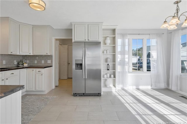 kitchen with stainless steel fridge, backsplash, white cabinets, decorative light fixtures, and a chandelier