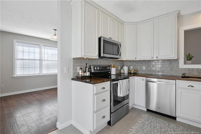 kitchen with stainless steel appliances, white cabinetry, light wood-type flooring, and decorative backsplash