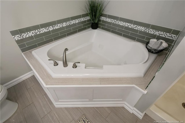 bathroom with toilet and tiled tub