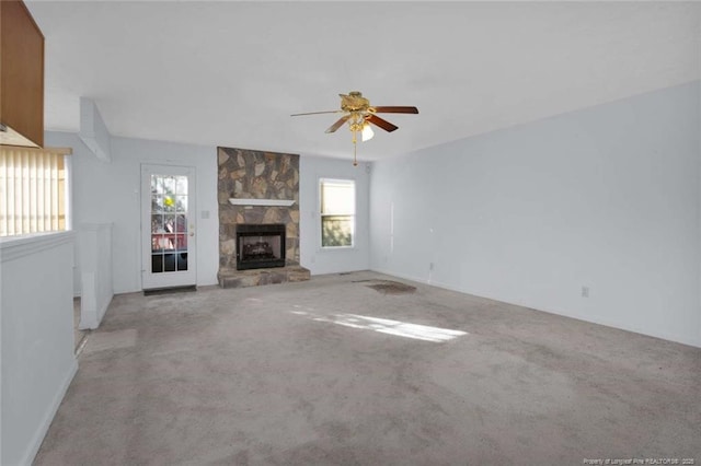 unfurnished living room featuring light carpet, a stone fireplace, and ceiling fan