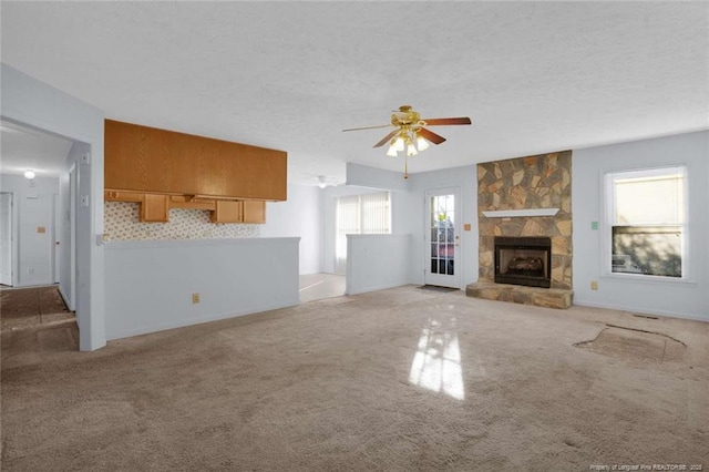 unfurnished living room featuring ceiling fan, light colored carpet, a textured ceiling, and a fireplace