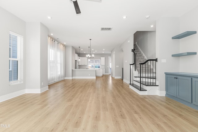 unfurnished living room with ceiling fan with notable chandelier and light wood-type flooring