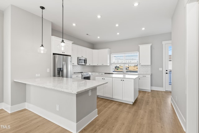 kitchen with appliances with stainless steel finishes, decorative light fixtures, white cabinets, light stone counters, and kitchen peninsula