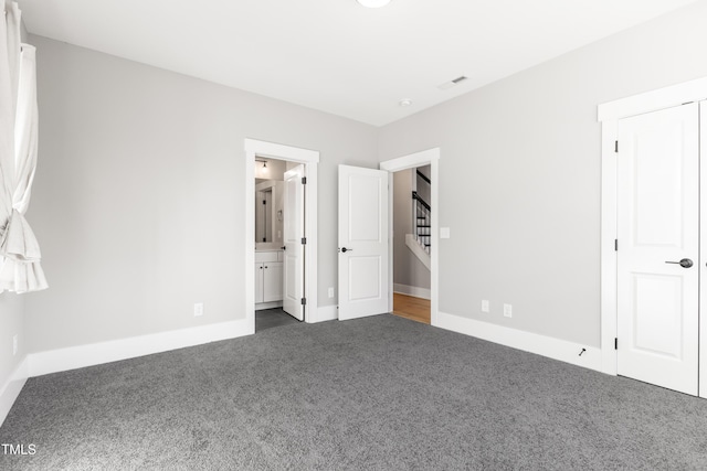 unfurnished bedroom with ensuite bathroom and dark colored carpet