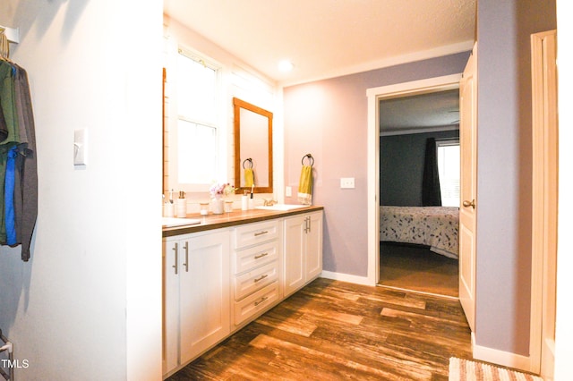 bathroom with ensuite bathroom, double vanity, wood finished floors, and baseboards