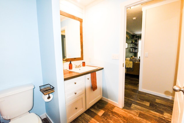 half bath featuring toilet, connected bathroom, vanity, wood finished floors, and baseboards