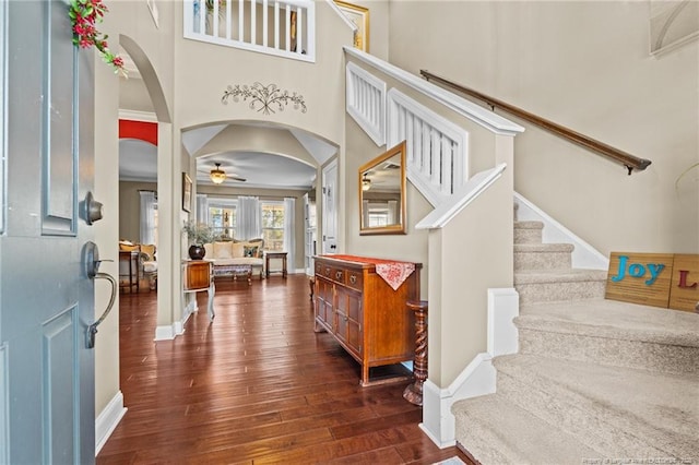 foyer entrance with dark wood-type flooring, ceiling fan, and a towering ceiling