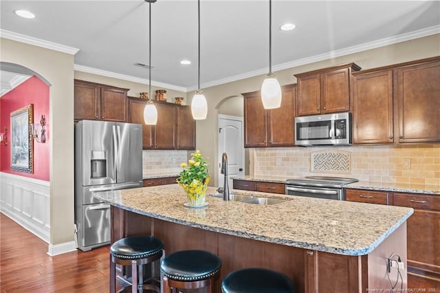 kitchen with decorative light fixtures, an island with sink, sink, stainless steel appliances, and light stone countertops