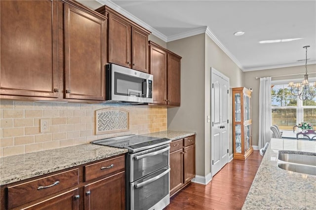 kitchen featuring crown molding, a notable chandelier, pendant lighting, stainless steel appliances, and light stone countertops