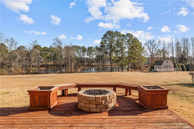 wooden terrace featuring a fire pit, a lawn, and a water view