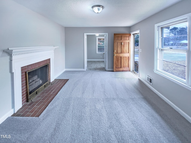 unfurnished living room featuring a brick fireplace, carpet floors, and a textured ceiling