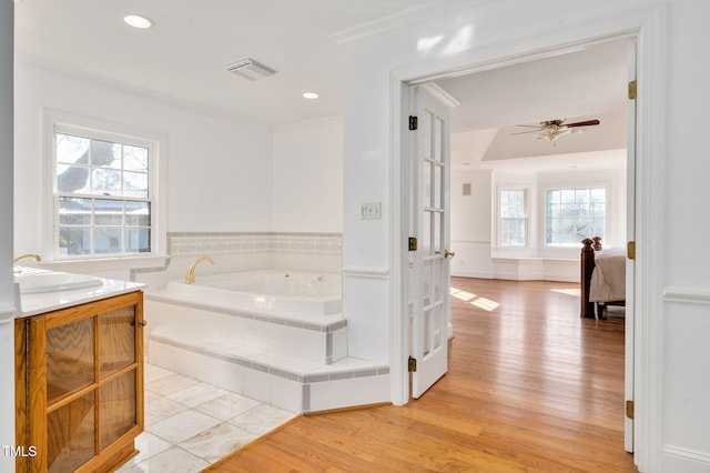 bathroom featuring tiled tub, crown molding, ceiling fan, vanity, and wood-type flooring