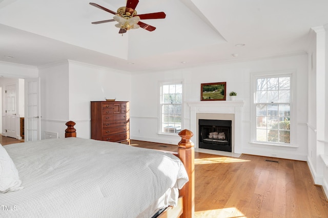 bedroom with ceiling fan, ornamental molding, a tray ceiling, and light wood-type flooring