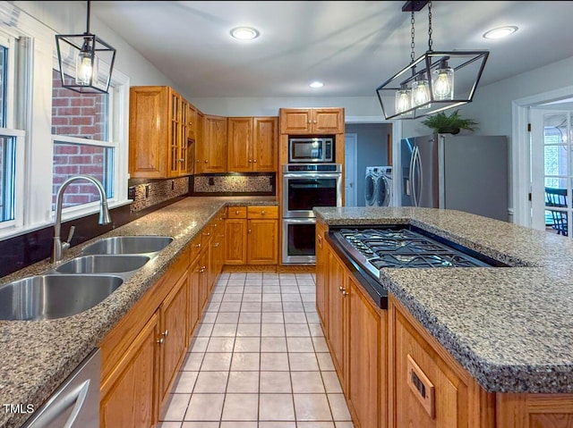 kitchen with a kitchen island, decorative light fixtures, sink, stainless steel appliances, and washing machine and dryer