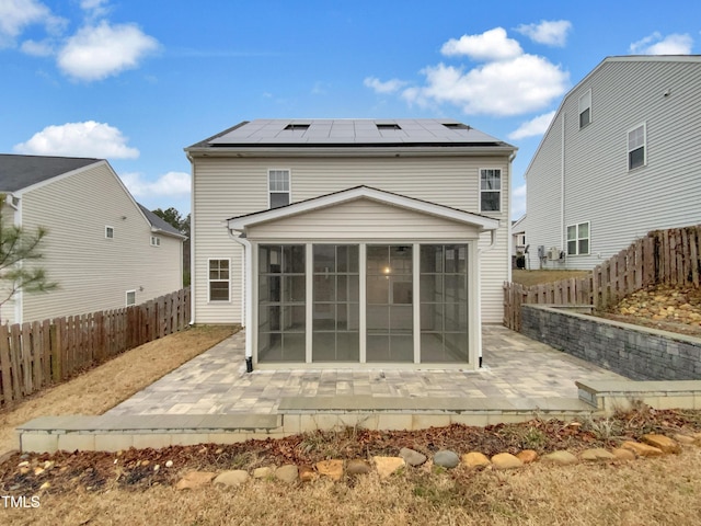 rear view of property featuring a patio area, a sunroom, and solar panels