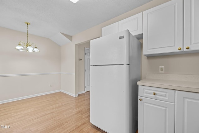 kitchen with pendant lighting, light wood-type flooring, white cabinets, white refrigerator, and an inviting chandelier