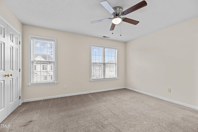 carpeted spare room with ceiling fan, a textured ceiling, and a wealth of natural light