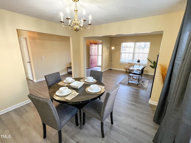 dining space with a textured ceiling, an inviting chandelier, wood finished floors, and baseboards