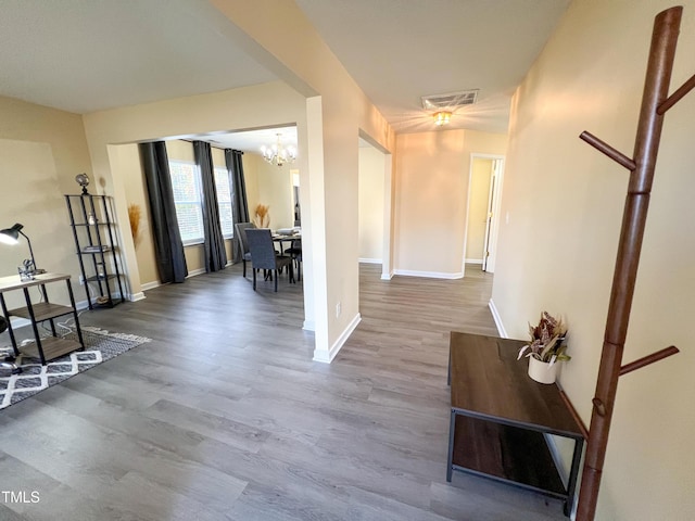 corridor with a notable chandelier, wood finished floors, visible vents, and baseboards