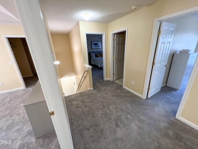 hall with dark carpet and a textured ceiling