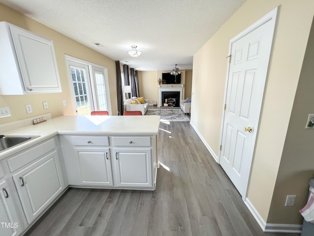 kitchen with wood finished floors, a peninsula, a textured ceiling, a fireplace, and white cabinetry