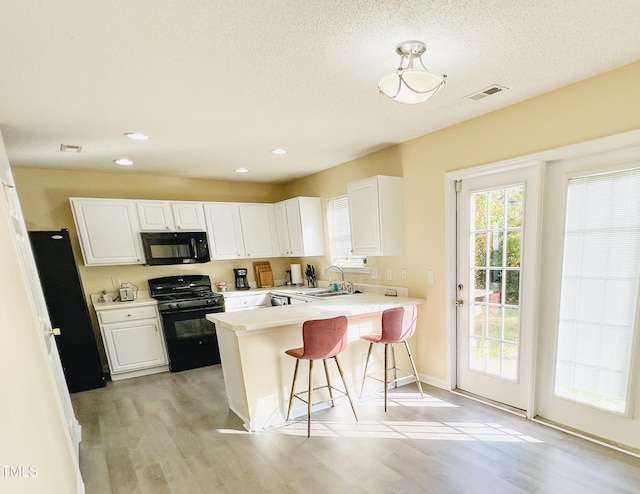 kitchen with visible vents, a peninsula, black appliances, white cabinetry, and a sink