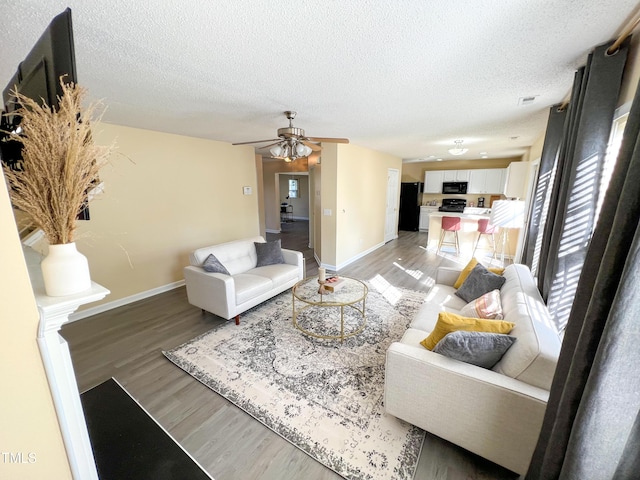 living room with light wood-style floors, ceiling fan, baseboards, and a textured ceiling