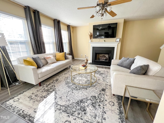 living room featuring a textured ceiling, ceiling fan, a fireplace, wood finished floors, and baseboards