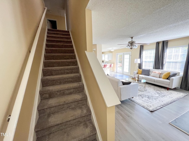 staircase with a ceiling fan, a textured ceiling, baseboards, and wood finished floors