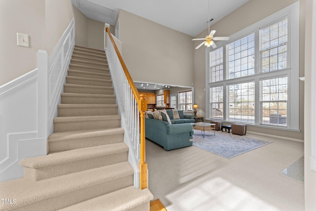 stairway with carpet, a healthy amount of sunlight, ceiling fan, and a towering ceiling