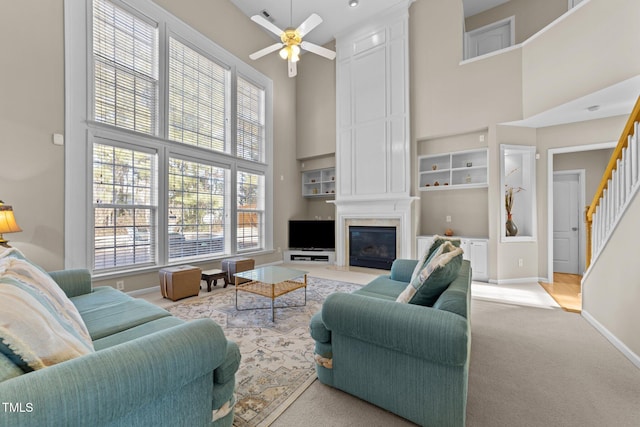 carpeted living room featuring ceiling fan, a towering ceiling, a large fireplace, and built in features