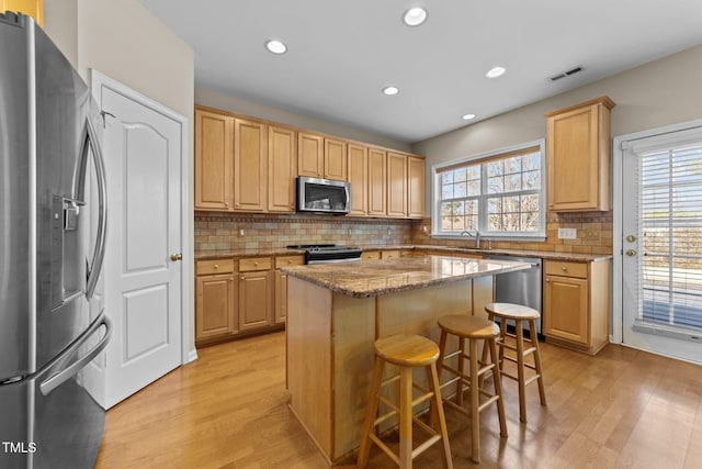 kitchen with appliances with stainless steel finishes, light brown cabinetry, a breakfast bar area, a center island, and light hardwood / wood-style floors