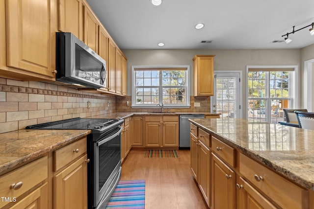 kitchen with sink, light wood-type flooring, stainless steel appliances, light stone countertops, and decorative backsplash