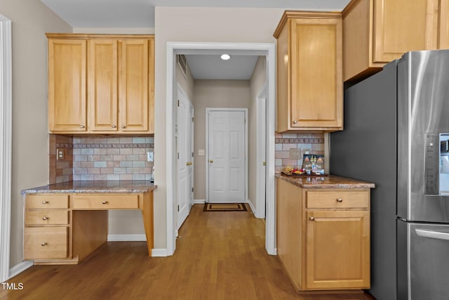 kitchen with backsplash, light stone countertops, light brown cabinetry, stainless steel fridge with ice dispenser, and light wood-type flooring