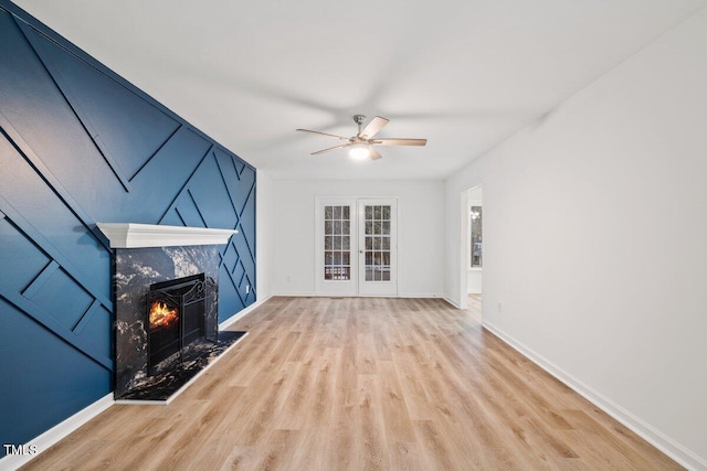 unfurnished living room with french doors, ceiling fan, a fireplace, and light wood-type flooring